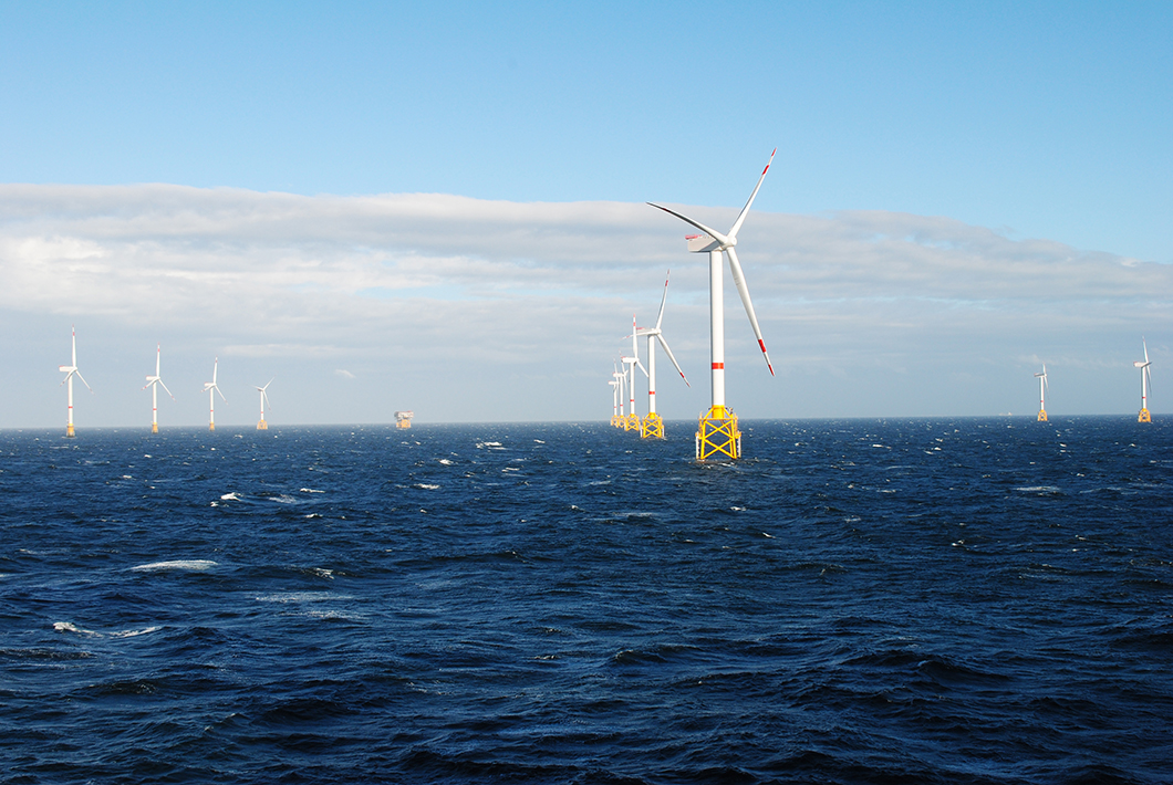 Offshore wind turbines with yellow bases are spaced across the sea, generating renewable energy under a partly cloudy sky.