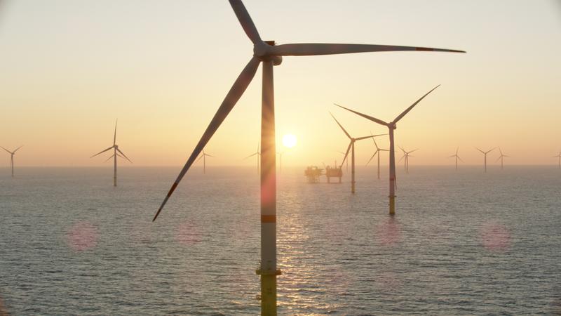 Offshore wind turbines stand in the ocean at sunset, generating renewable energy as the sun sets on the horizon.