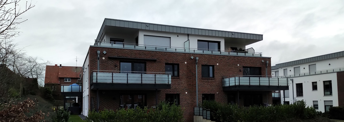 Ein modernes zweistöckiges Apartmentgebäude aus Backstein und Weiß mit Balkonen, großen Fenstern und einem Flachdach in einem Wohngebiet unter einem bewölkten Himmel.