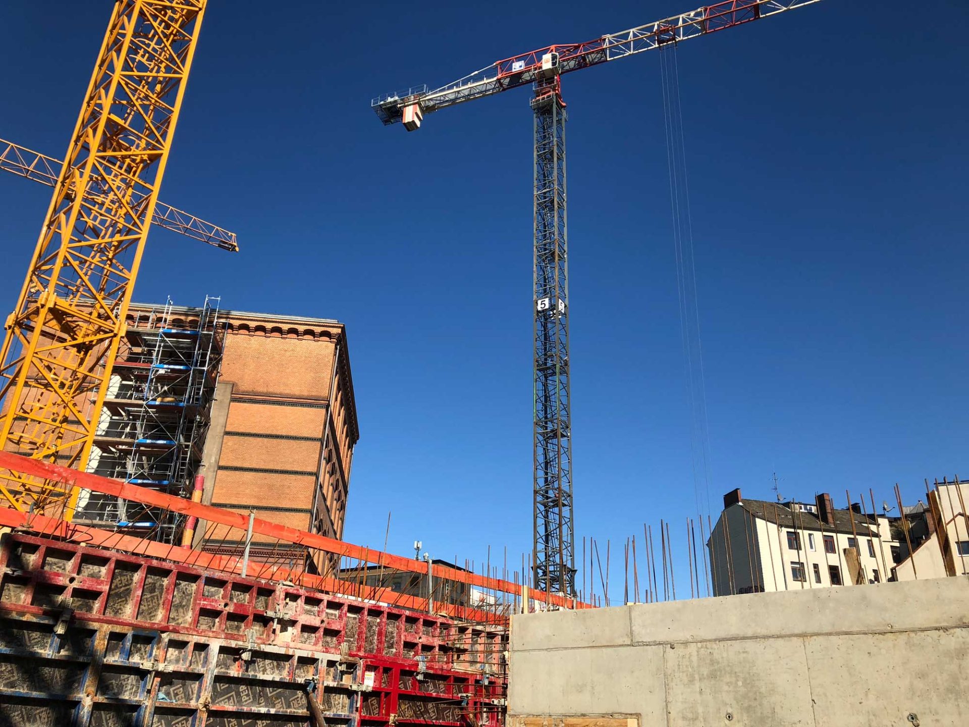 Construction site with scaffolding, cranes, and reinforced concrete structures under a clear blue sky.