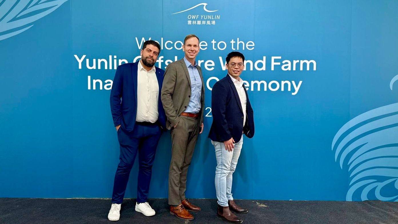 Drei Männer in Geschäftskleidung stehen vor einem blauen Hintergrund mit der Aufschrift „Willkommen zur Eröffnungszeremonie des Offshore-Windparks Yunlin Taiwan“.